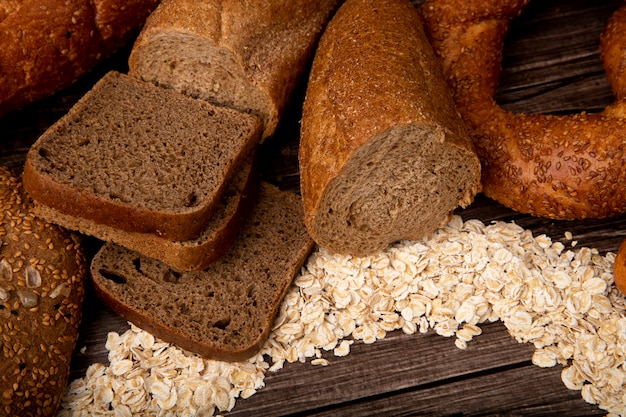 Foto gratuita la vista laterale dei pani come pane di segale affettato ha tagliato in mezzo bagel delle baguette con i fiocchi di avena su fondo di legno