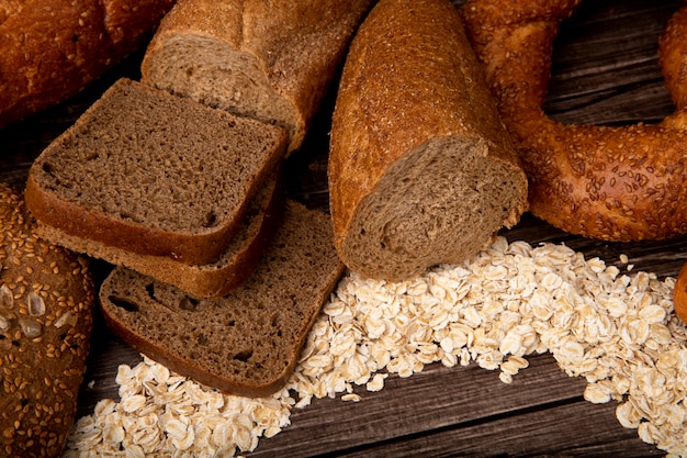 Side view of breads as sliced rye bread cut in half baguette bagel with oat-flakes on wooden background