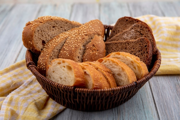 Side view of breads as sliced seeded brown cob rye and crusty ones in basket on plaid cloth on wooden background