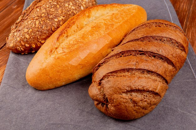 side view of breads as vietnamese and black seeded baguette and black bread on gray cloth and wooden table