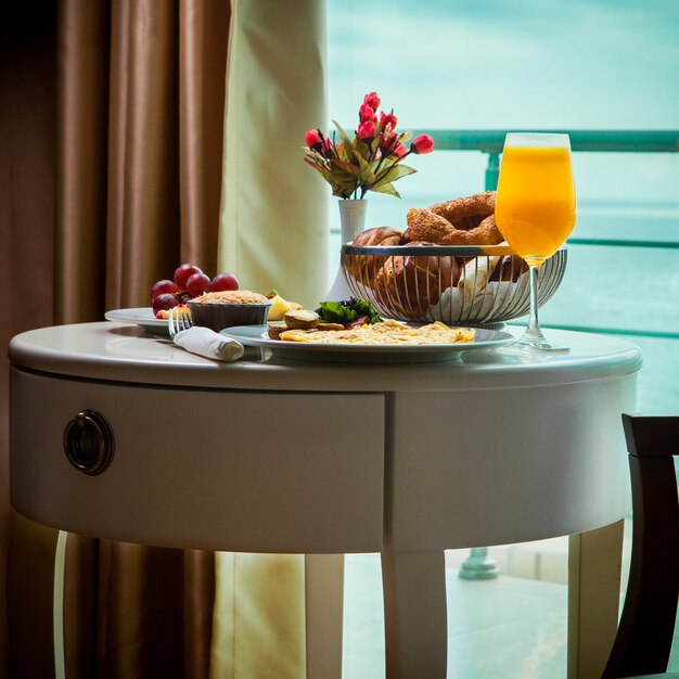 Side view breakfast omelet with mushrooms, juice, croissants in room service at hotel with amazing sea view