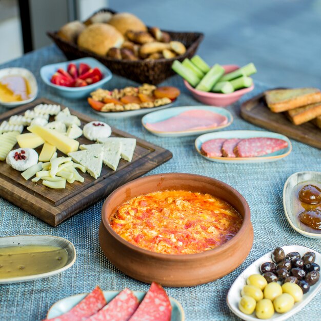 Side view of breakfast table served with various food fried eggs with tomatoes sausages cheese fresh salad dessert and tea