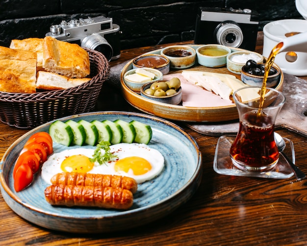 Side view of breakfast table with fried egg and sausages cheese ham and vegetables