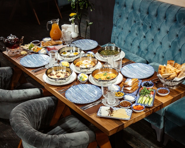 Side view of a breakfast table with various food fried eggs assorted ham fresh salad and juice