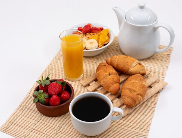Side view of breakfast with cornflakes, strawberries, juice and croissants on white surface horizontal