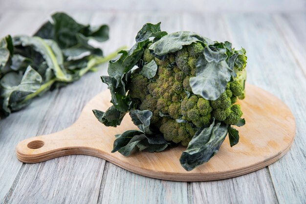 Side view of broccoli and broccoli leaves on cutting board and on wooden background