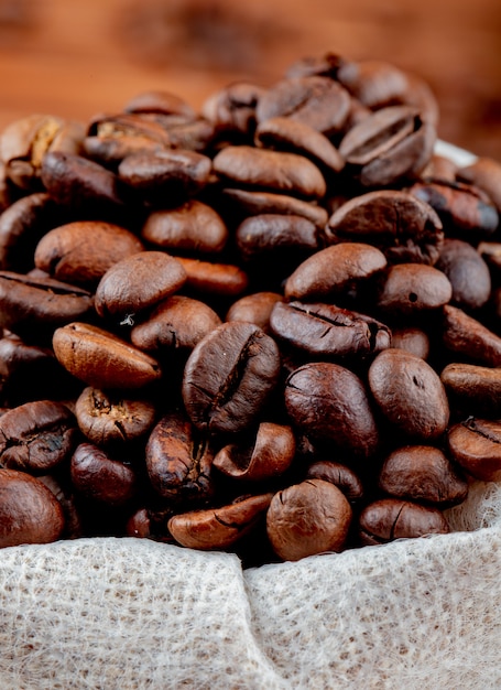 Side view of brown coffee beans in a sack on rustic table