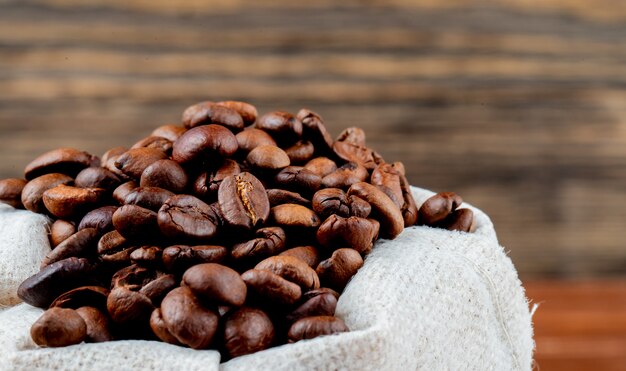 Side view of brown coffee beans in a sack on rustic table