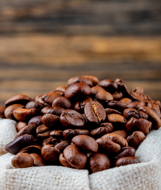 Side view of brown coffee beans in a sack on rustic table