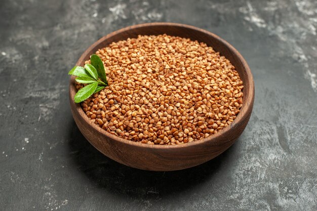 Side view of buckwheat groats with green in a brown bowl on gray background