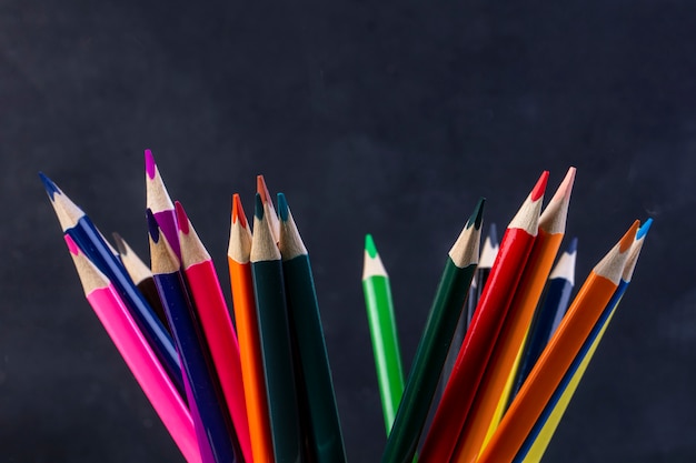 Вид сбоку кучу цветных карандашей на темном