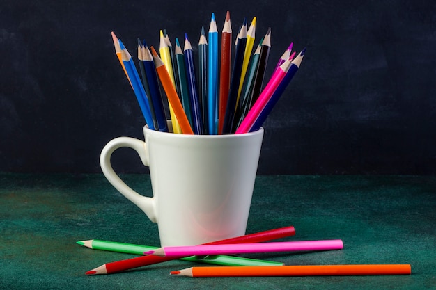 Side view of a bunch of colored pencils in a white cup on dark
