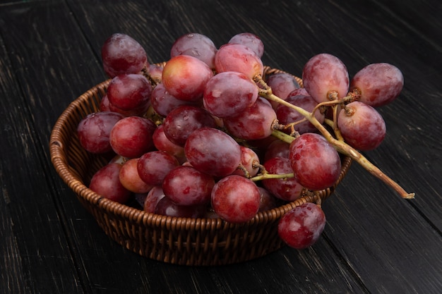 Вид сбоку гроздь свежего сладкого винограда в плетеной корзине на темном деревянном столе