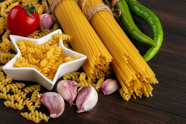 Side view of bunches of raw pasta with garlic and pasta with tomato and hot pepper on a wooden surface