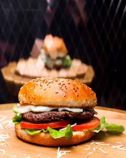 Side view of burger with beef meat melted cheese and vegetables on wooden board