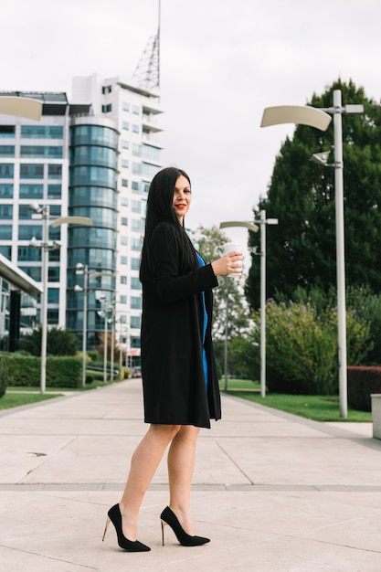 Side view of a businesswoman with disposal cup standing in front of building