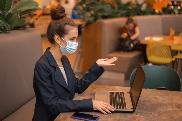 Side view businesswoman with medical mask working on her laptop