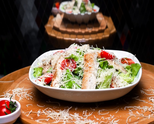 Side view of caesar salad with chicken and parmesan cheese in a white bowl on wooden board