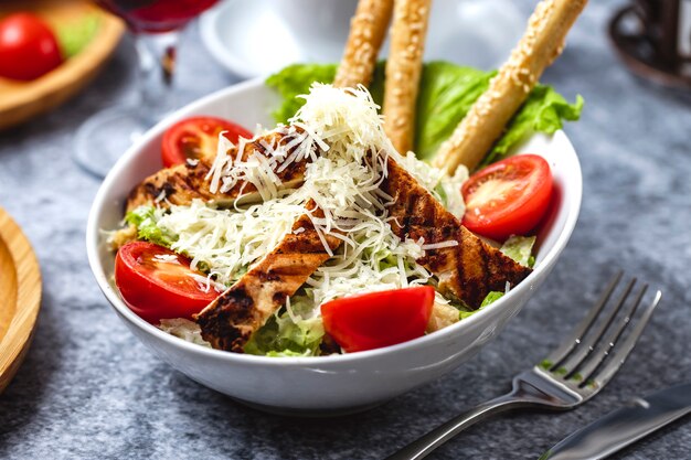 Side view caesar salad with grilled chicken parmesan tomato lettuce and bread sticks