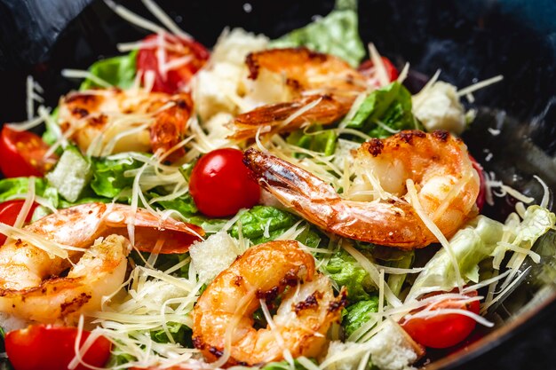 Side view caesar salad with grilled shrimps lettuce cherry tomatoes and parmesan on a plate