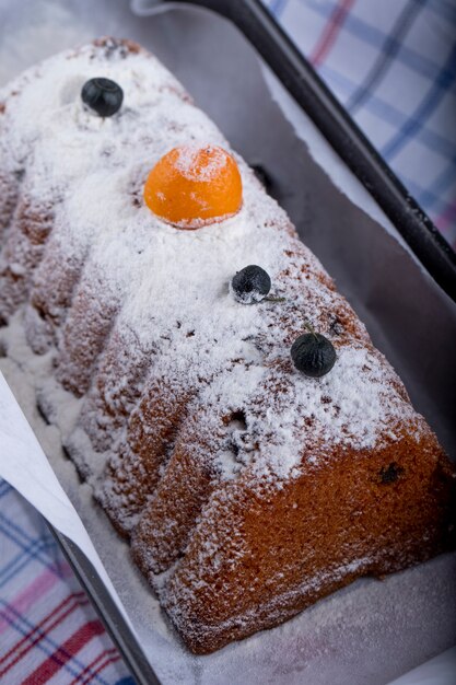 Side view of cake with raisins and powdered sugar on a black tray