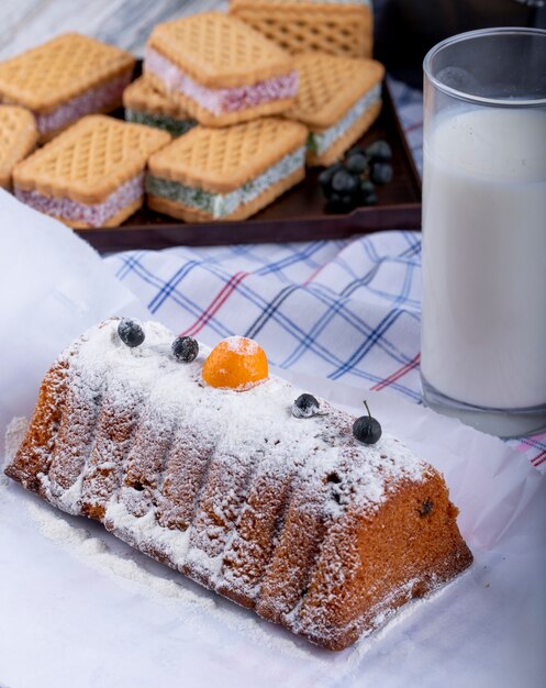 Side view of cake with raisins and powdered sugar and a glass of milk on the tablecloth
