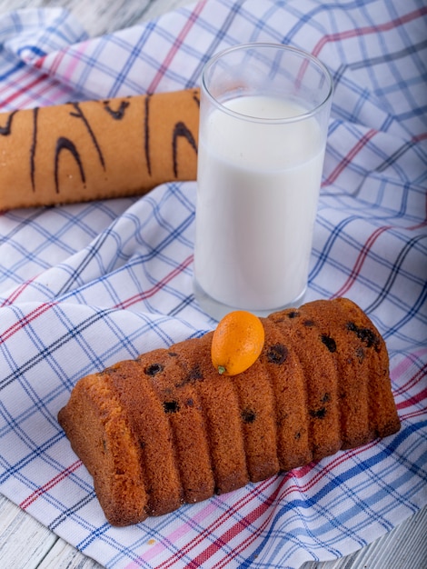 Vista laterale della torta con uvetta con kumquat e un bicchiere di latte sulla tovaglia