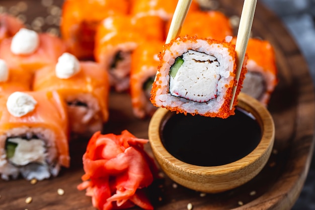 Side view california roll with crab meat cucumber tobiko caviar ginger and soy sauce on a board