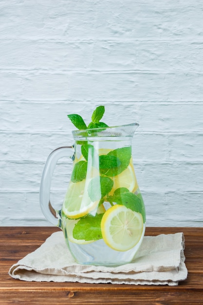 Side view carafe of lemon on white cloth on wooden and white surface. vertical space for text