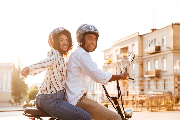 Free photo side view of carefree young african couple rides on modern motorbike on the street