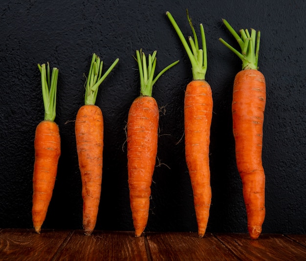 Free photo side view of carrots on wooden surface and black background