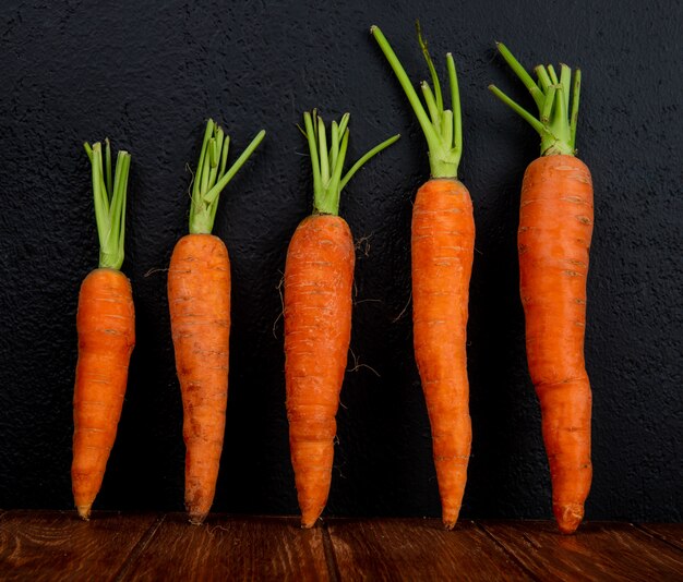 Side view of carrots on wooden surface and black background