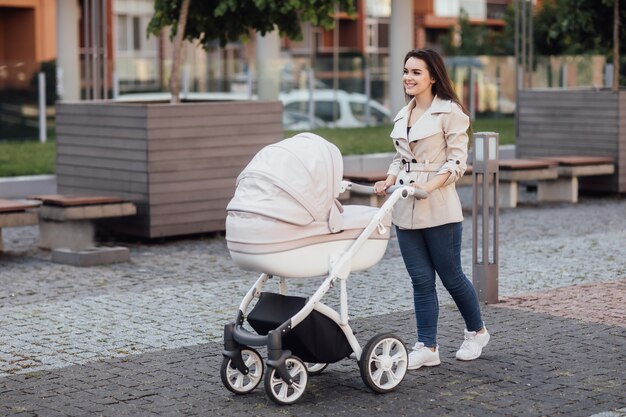 乳母車に座っている彼女の幼児を押しながら街の通りを歩いている白人の母の側面図