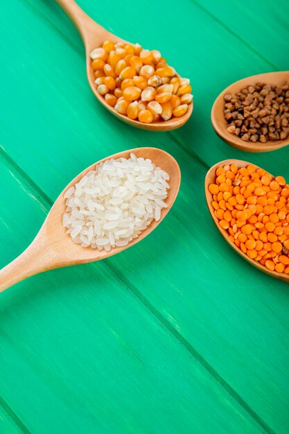 녹색 테이블에 나무 숟가락 옥수수 쌀 메밀과 빨간 렌즈 콩에 시리얼 곡물과 씨앗의 측면보기