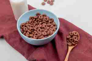 Free photo side view of cereals in bowl and in wooden spoon with milk on bordo cloth and white surface