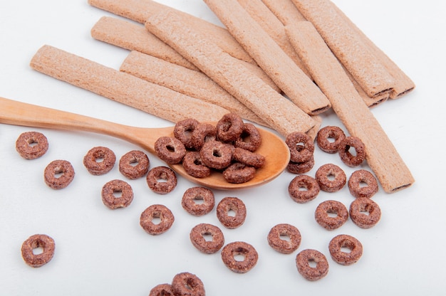 Side view of cereals in wooden spoon and cookies on white surface