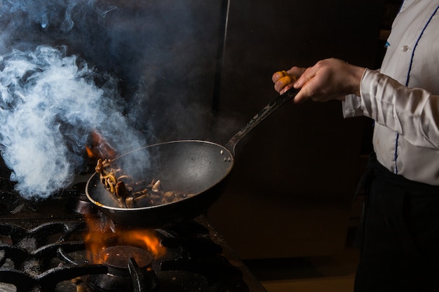 Side view champignon frying with smoke and fire and human in stove