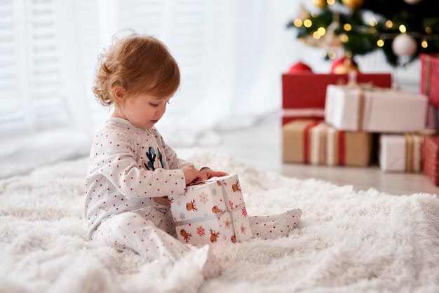 Очаровательный ребенок, открывающий рождественский подарок, вид сбоку