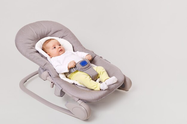 Side view of charming new born girl lying in bounce child bouncer chair