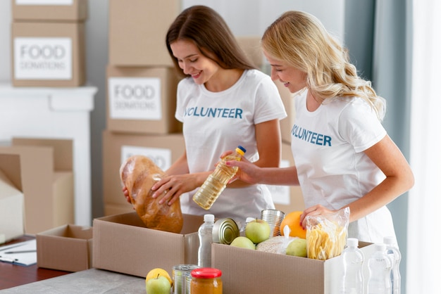 Free photo side view of cheerful female volunteers preparing food donations