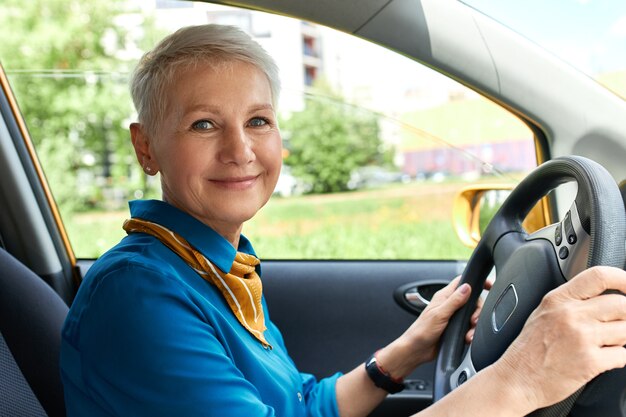Side view of cheerful middle aged woman inside car on driver's seat with hands on steering wheel