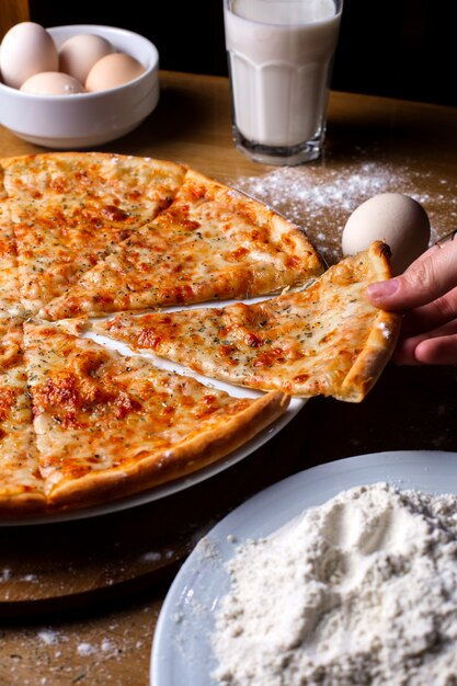 Side view cheese pizza with eggs a glass of milk and flour on the table