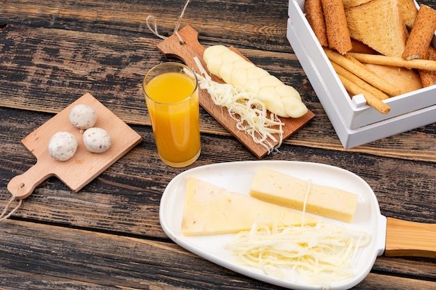 Side view of cheese with toasts, crackers and juice on dark wooden surface horizontal