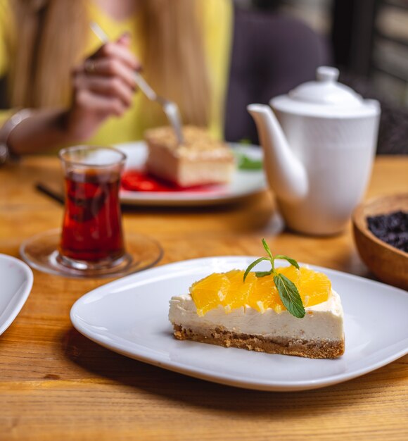 Side view of cheesecake served with orange slices on a white plate