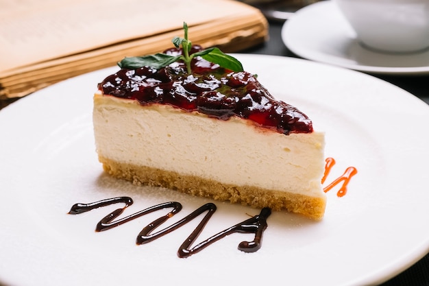 Foto gratuita vista laterale della cheesecake con gelatina di ciliegie sulla parte superiore su un piatto bianco