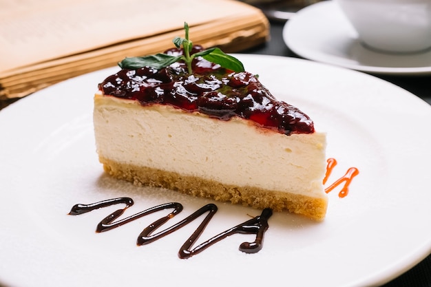 Side view of cheesecake with cherry jelly on the top on a white plate