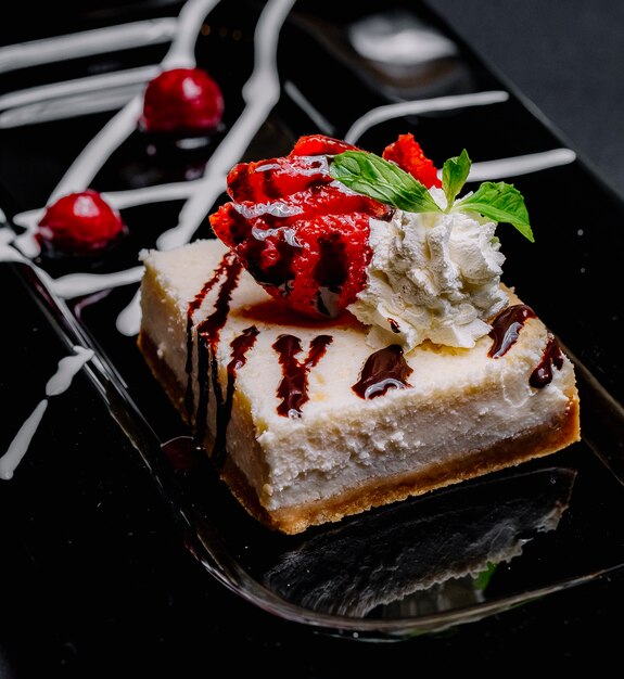 Side view cheesecake with chocolate whipped cream strawberry mint and cherry on a plate