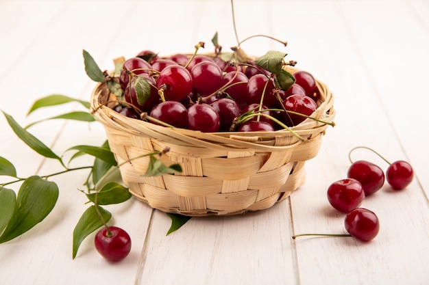 Side view of cherries in basket with leaves on wooden background