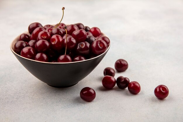 Side view of cherries in bowl and on white background