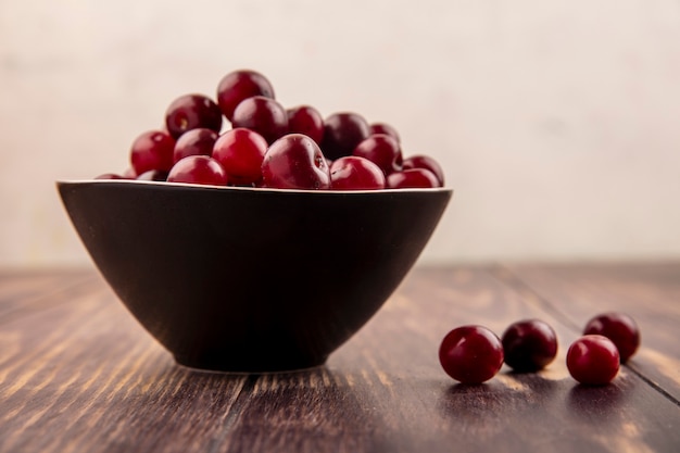 Side view of cherries in bowl and on wooden surface and white background